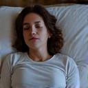 Woman performing progressive muscle relaxation in bed before sleep, looking peaceful.